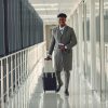 A young stylish man with suitcase and passport walking along airport corridor